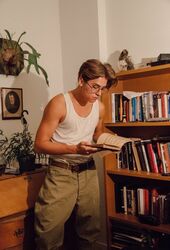  1boy atlantis belt book bookshelf cosplay desk disney glasses male_focus milo_thatch photo picture_frame potted_plant reading shelf tank_top theodore_roosevelt 