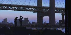  2girls alzi_xiaomi arms_behind_back blue_sky blurry blurry_foreground bridge building city dusk from_behind full_body highres lamppost long_hair multiple_girls original outdoors scenery shirt short_hair silhouette skirt sky skyline standing 