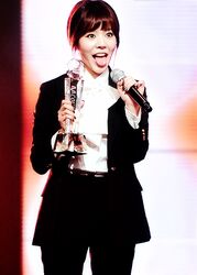  black_pants black_suit brown_hair female formal girls&#039;_generation k-pop microphone pants photo short_hair standing suit sunny_(girls&#039;_generation) tongue trophy 