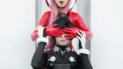  1boy bangs black_bodysuit black_hair blue_eyes bodysuit cosplay couple darling_in_the_franxx female gloves hair_ornament hairband hiro_(darling_in_the_franxx) hiro_(darling_in_the_franxx)_(cosplay) long_hair pilot_suit pink_hair red_bodysuit red_gloves straight white_gloves white_hairband zero_two_(darling_in_the_franxx) zero_two_(darling_in_the_franxx)_(cosplay) 