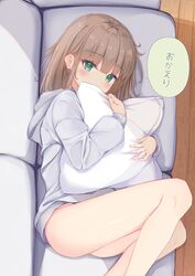  blush brown_hair commentary couch covered_mouth feet_out_of_frame female green_eyes grey_hoodie highres hood hood_down hoodie hugging_object indoors long_hair long_sleeves looking_at_viewer lying on_couch on_side original pillow pillow_hug sashima solo translated wooden_floor 