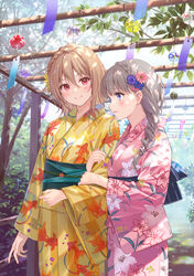  2girls animal_print blonde_hair blue_eyes blush brown_hair commentary_request fish_print floral_print fukahire_(ruinon) goldfish_print highres holding_another&#039;s_arm japanese_clothes kimono leaf lily_print long_hair long_sleeves looking_at_another medium_hair mole mole_under_eye multiple_girls obi obidome obijime original outdoors parted_lips pink_eyes pink_kimono sash shadow smile tree wide_sleeves wind_chime yellow_kimono yukata yuri 